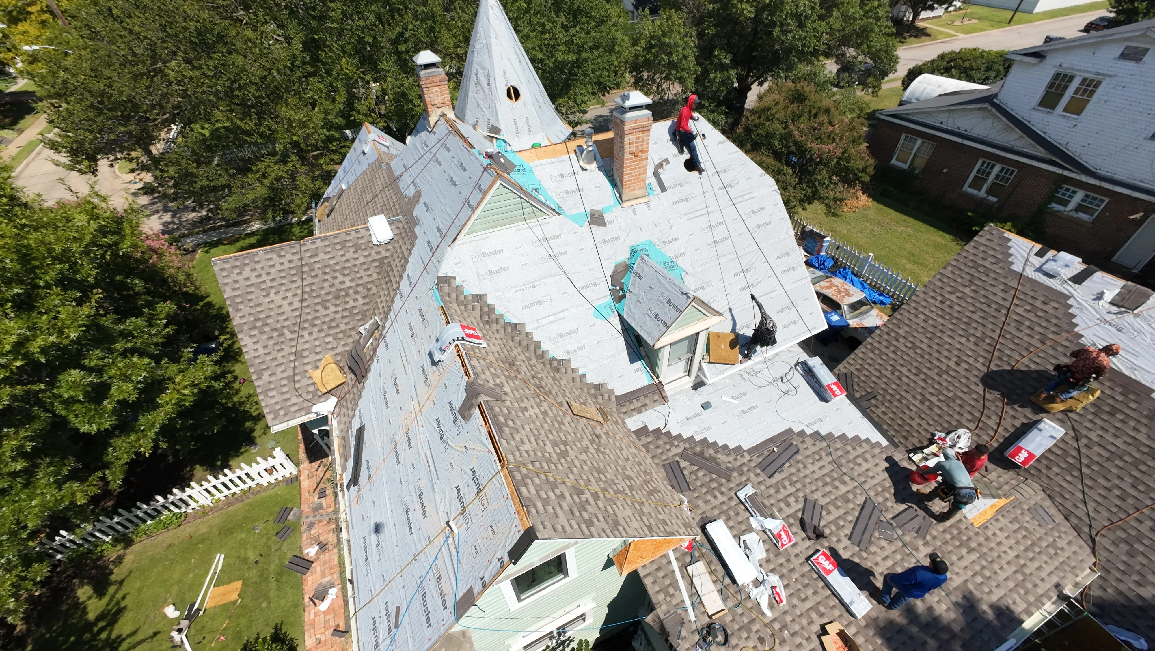 Aerial view of roof replacement in progress with new shingles, underlayment, and brick chimney