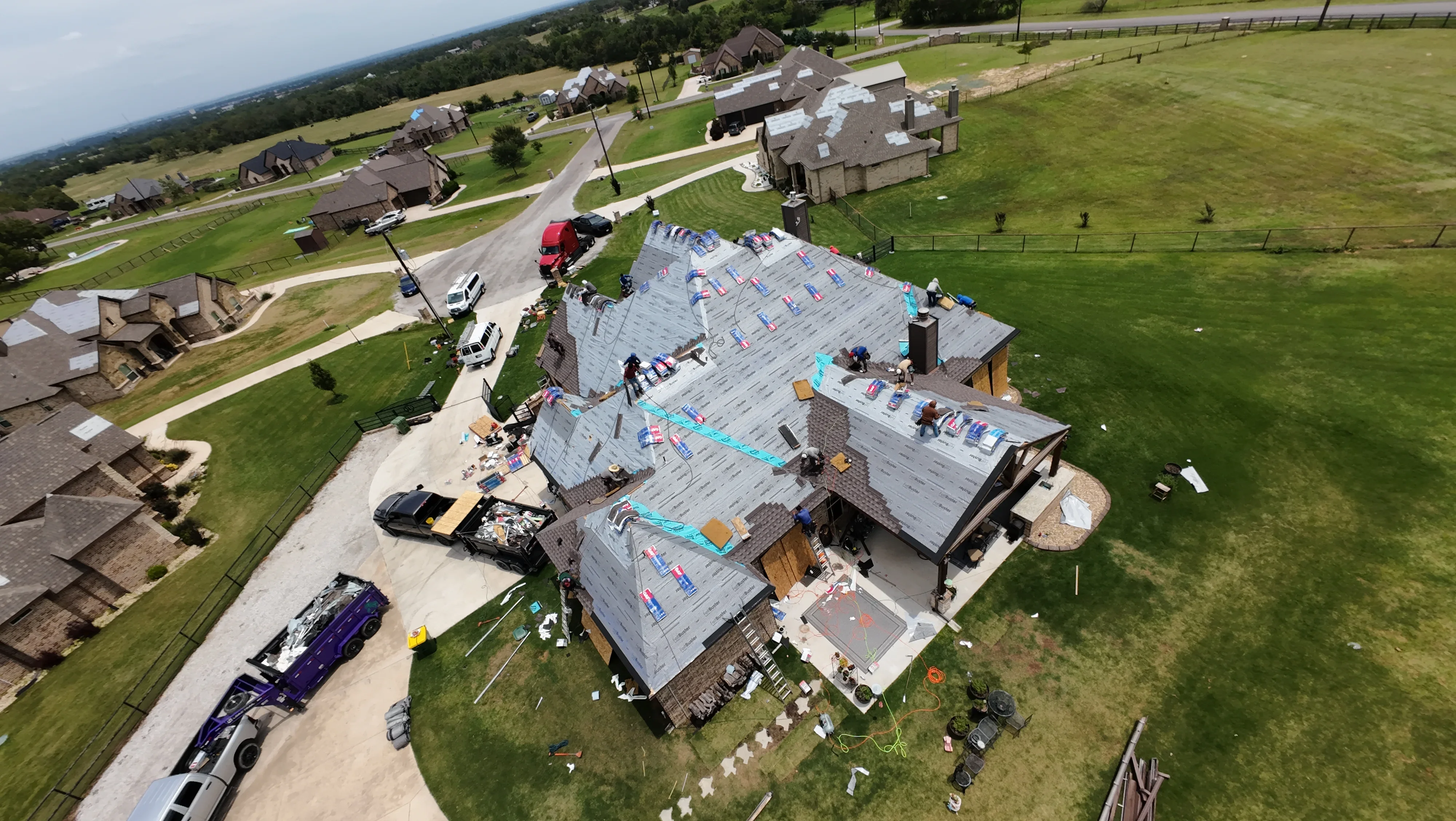 Aerial view of residential roof replacement with new underlayment, shingles, and brick chimney work in progress