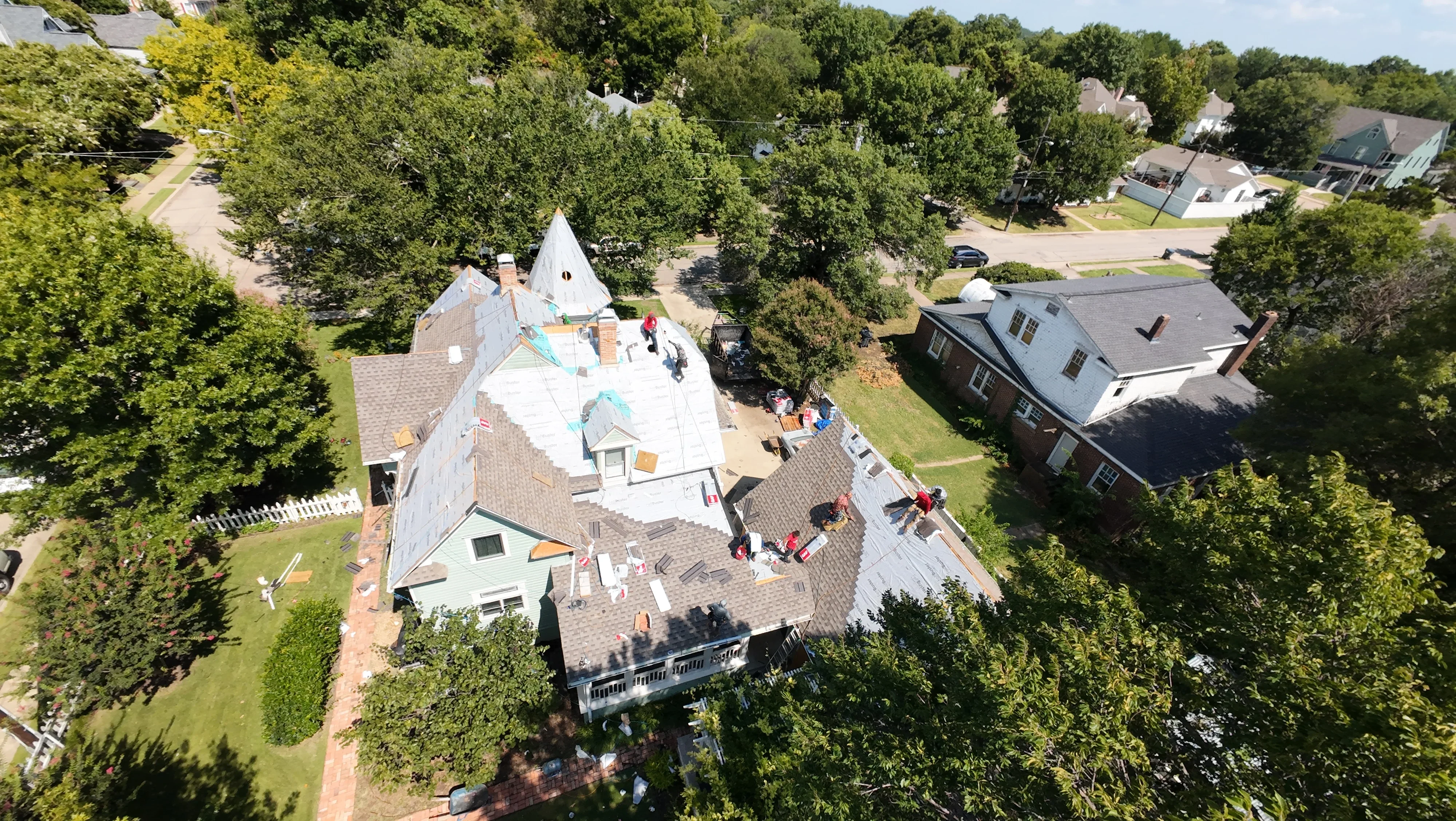 Aerial view of residential roof with new asphalt shingles, multiple peaks, and active installation crew