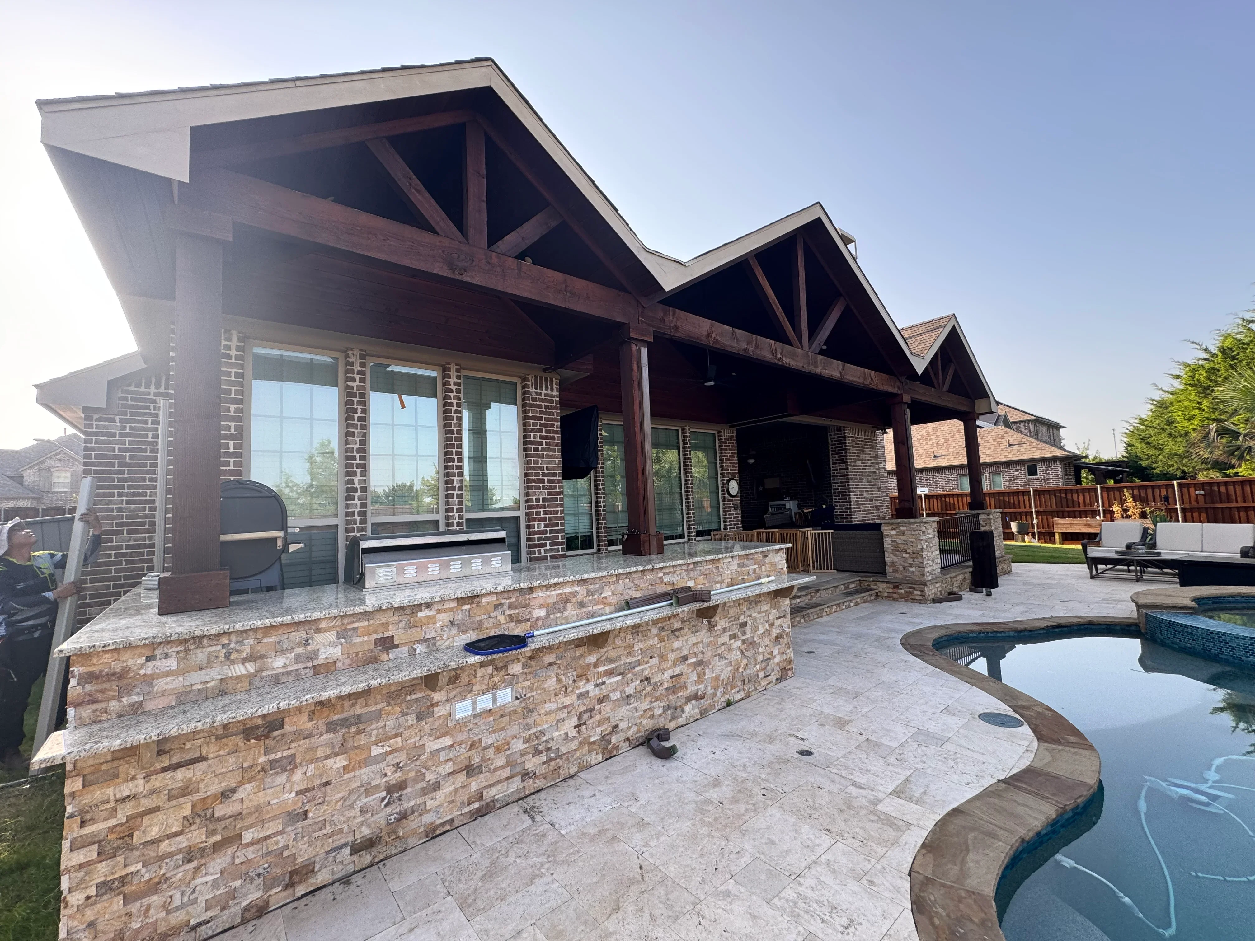 Patio cover with exposed wood beams, metal roof, stone veneer bar, and granite countertop